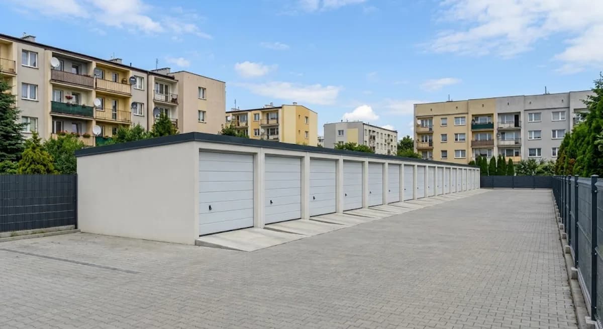 Rząd nowych boksów garażowych na ogrodzonym terenie w mieście, w tle bloki